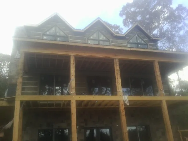 Dormers and porch framing on a large log home under construction — Roof Coating work by our crew in Buxton